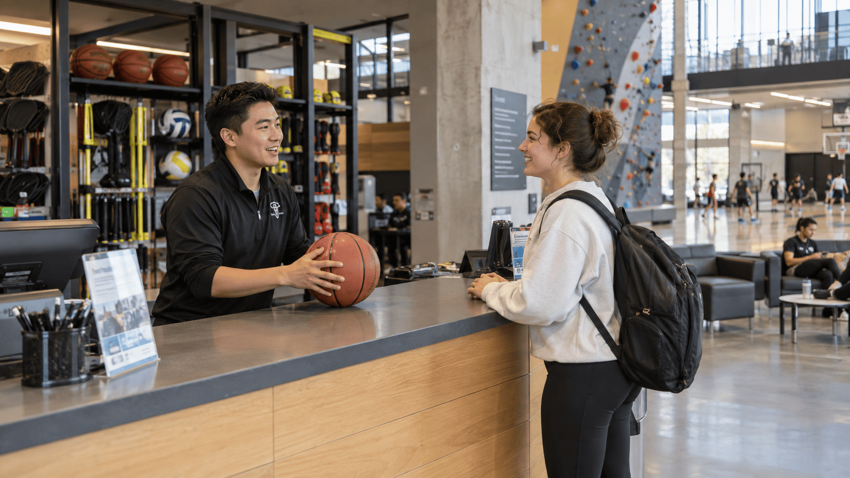 A student speaking with a staff member at a recreation center equipment desk.